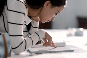 A reading girl is sitting on the ground and using the book to read while donning a white dress.