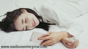 Using her phone to do her job, a phone actress is laying on the bed.