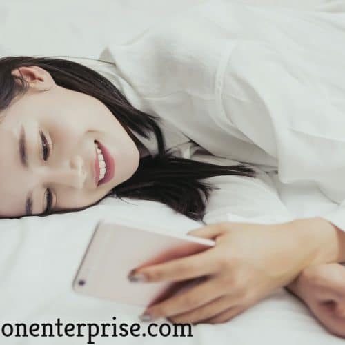 Using her phone to do her job, a phone actress is laying on the bed.