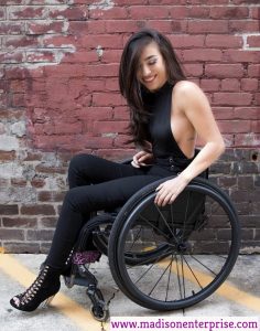 A woman working as a sex worker is seated in a wheelchair and wearing a black attire.