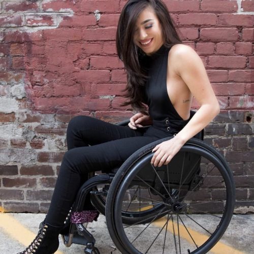A woman working as a sex worker is seated in a wheelchair and wearing a black attire.