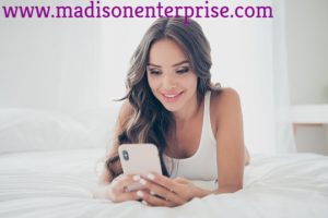 A phone sex operator is working on her cell while lying on the bed.