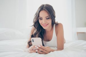 A phone sex operator is working on her cell while lying on the bed.